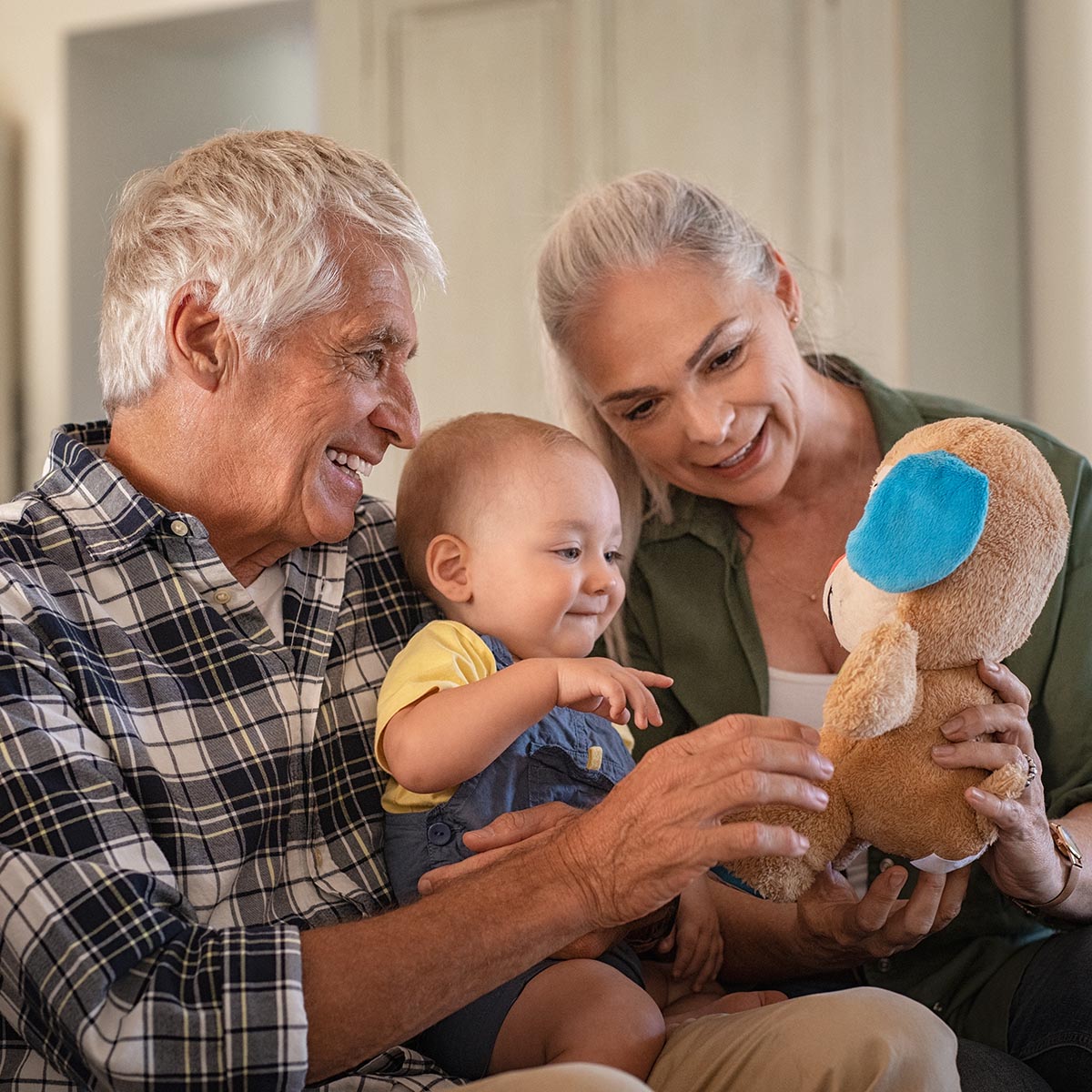 Toddler playing with old grandparents and teddy bear stuff toy.